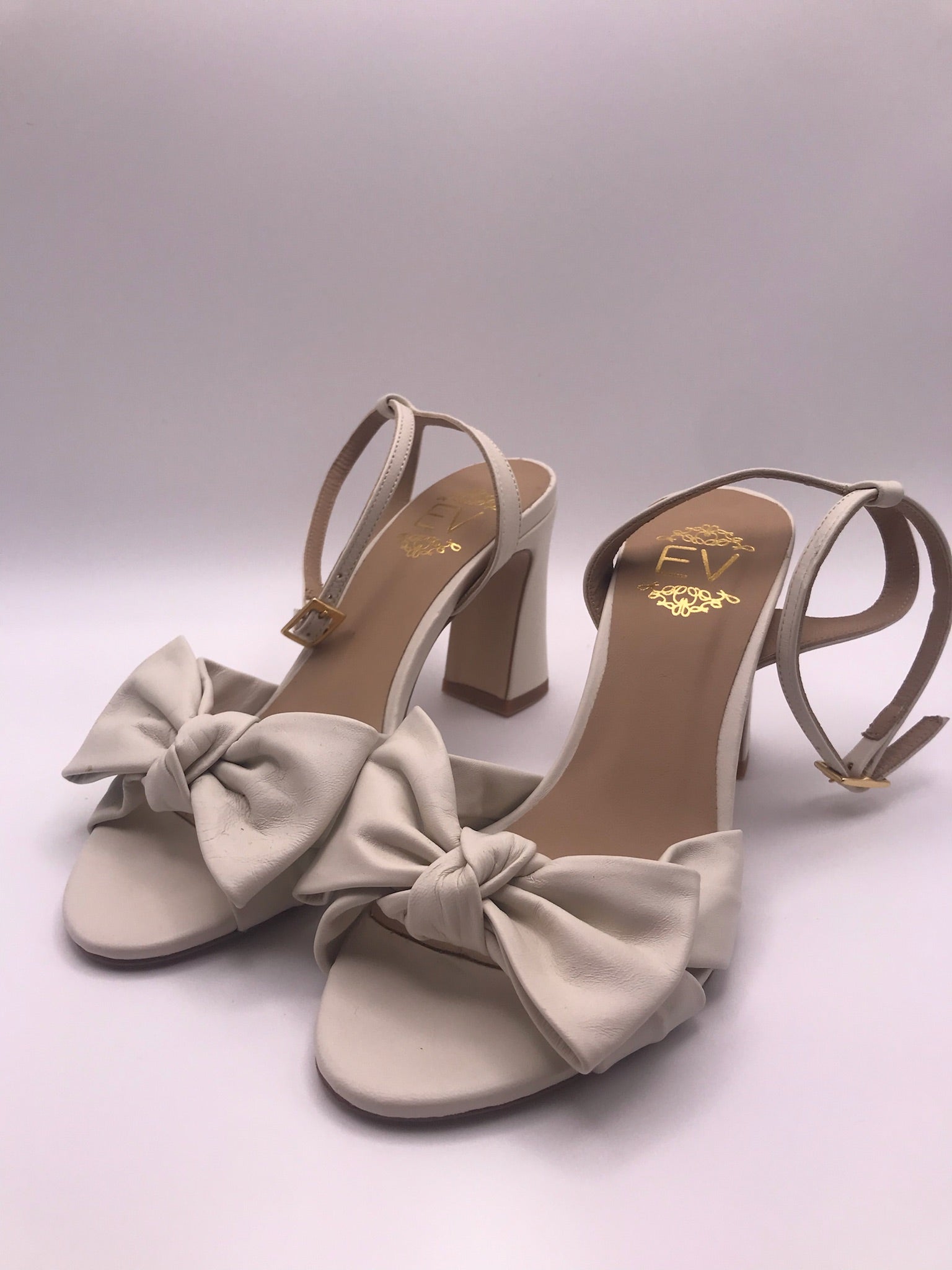 Sandálias de senhora em pele creme com laço frontal EV; sapatos de salto alto grosso com tira no tornozelo e fivela dourada; calçado elegante para noivas ou cerimónias especiais
