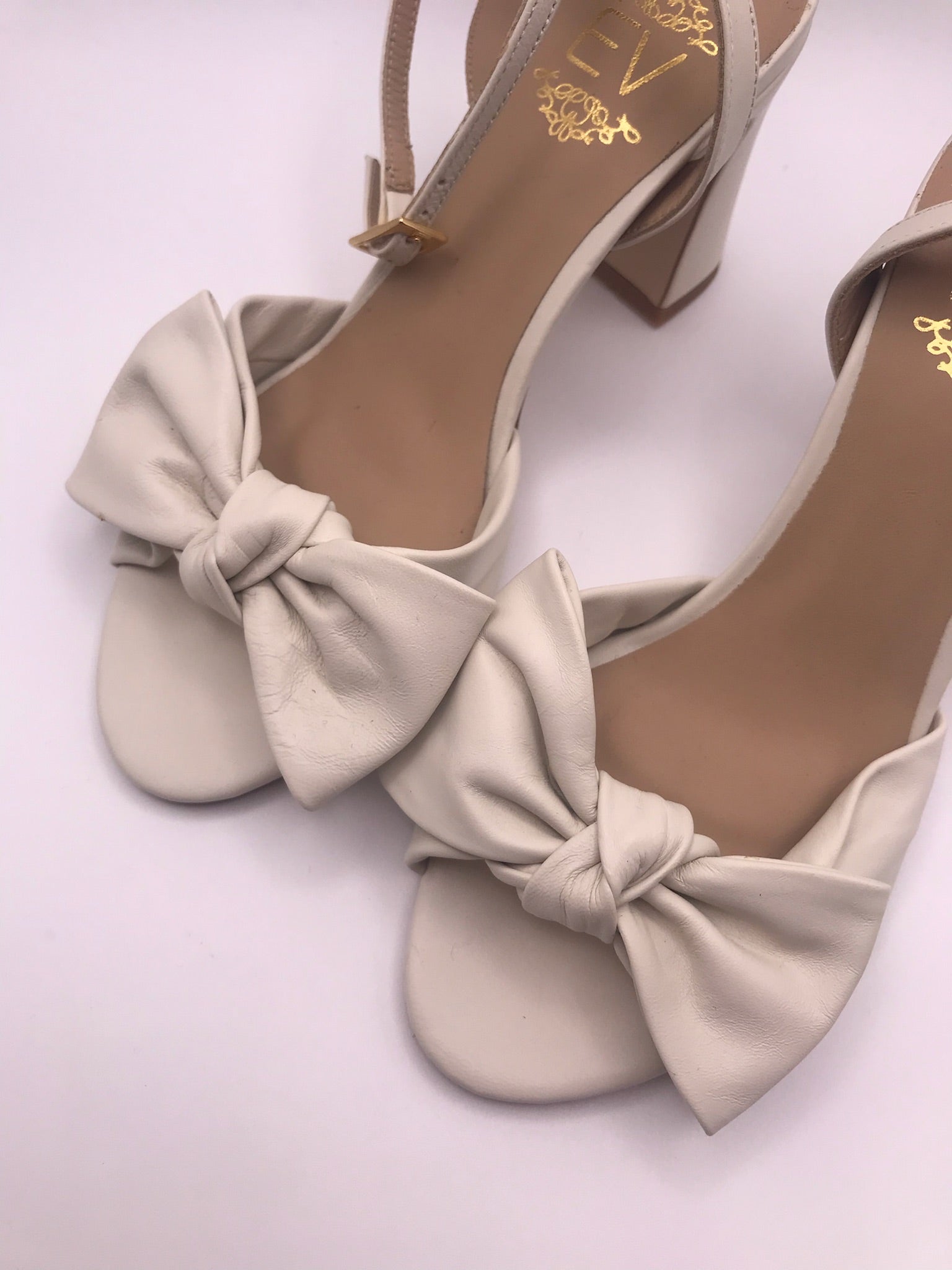 Sandálias de senhora em pele creme com laço frontal EV; sapatos de salto alto grosso com tira no tornozelo e fivela dourada; calçado elegante para noivas ou cerimónias especiais