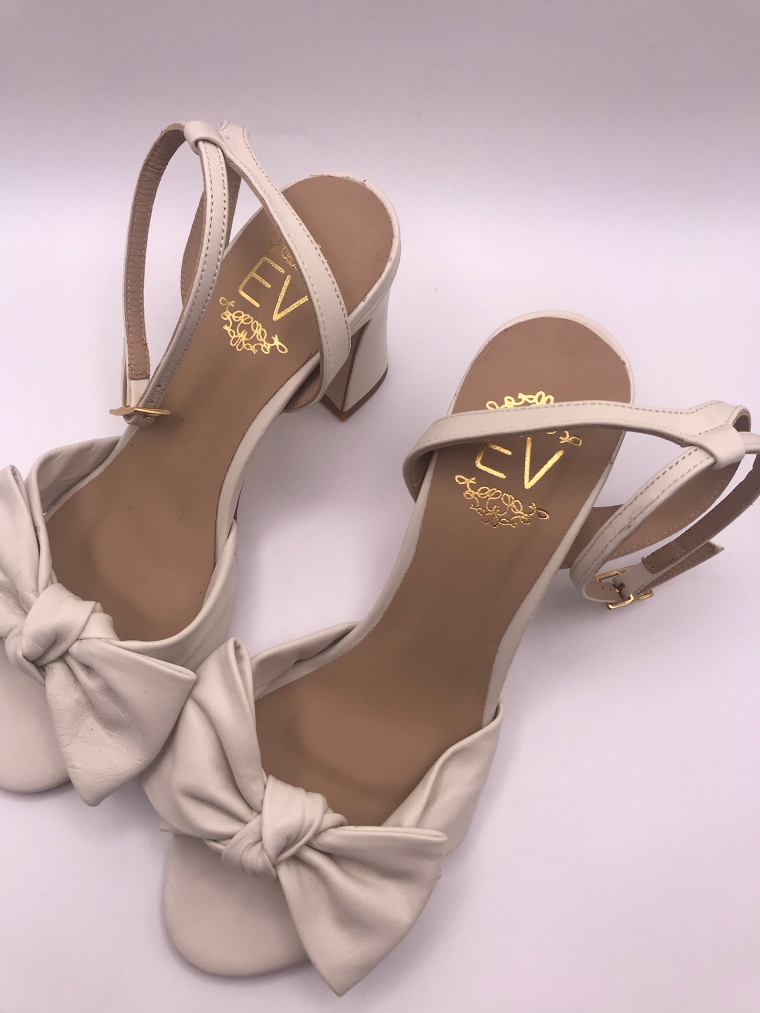Sandálias de senhora em pele creme com laço frontal EV; sapatos de salto alto grosso com tira no tornozelo e fivela dourada; calçado elegante para noivas ou cerimónias especiais